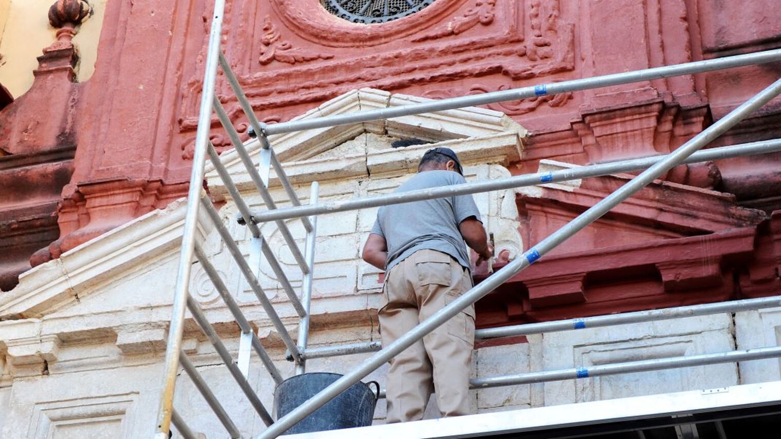 Denkmalpflege, Restaurierung. Mann auf Gerüst restauriert Fassade einer Kirche.