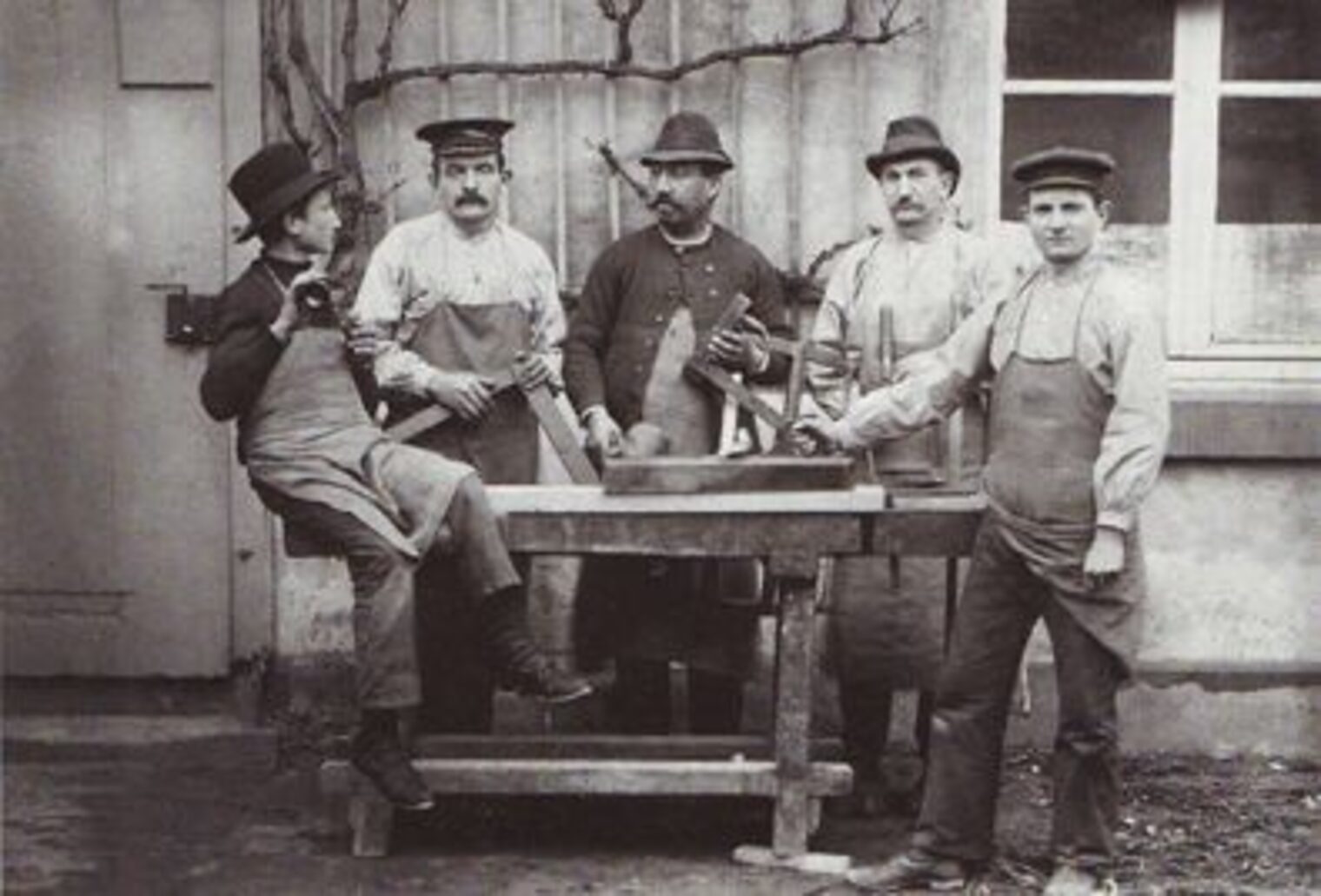 Historisches Foto aus dem Jahr 1902. Fünf Schreiner stehen an einer Hobelbank