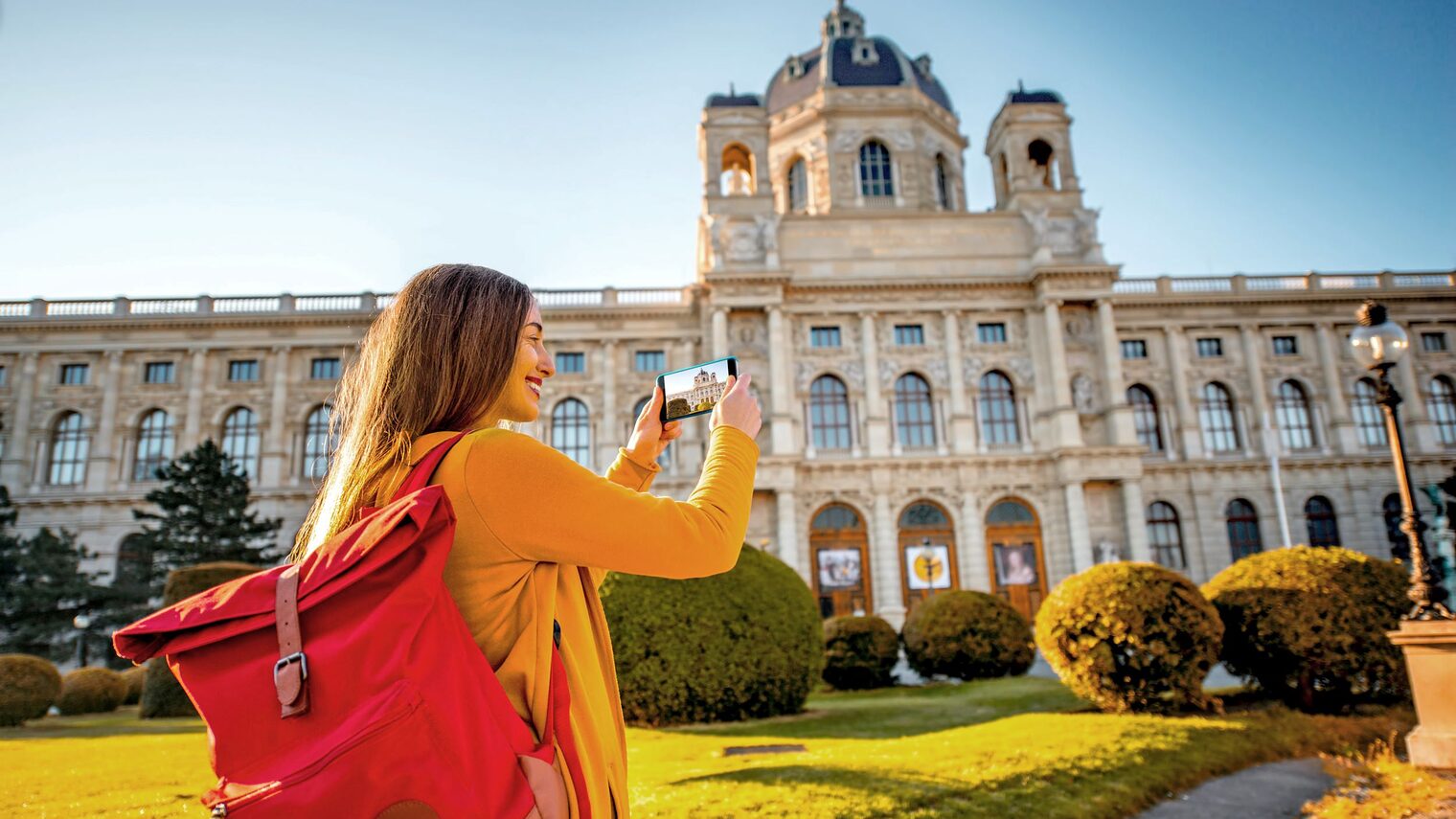 Junge Frau mit Rucksack fotografiert die Wiener Hofburg mit ihrem Handy.