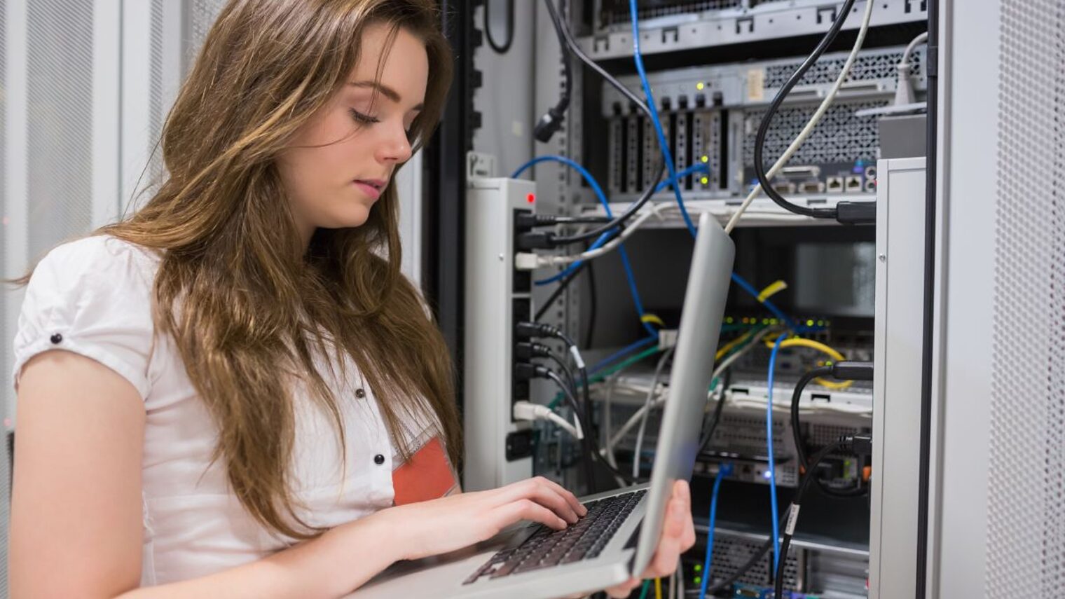 Junge Frau, die Laptop verwendet, um auf Servern im Rechenzentrum zu arbeiten.