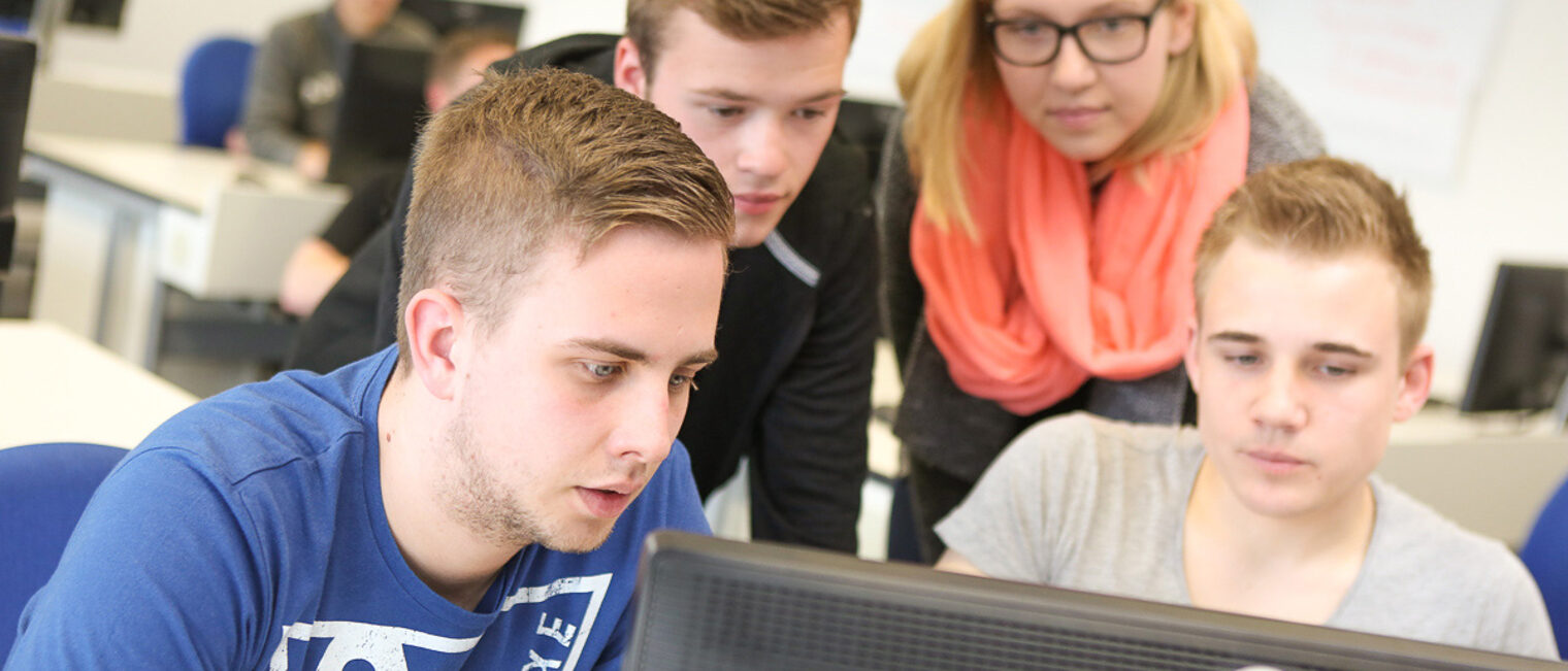 Teamarbeit im Seminar – Teilnehmer diskutieren eine Aufgabe am Computer Gruppe von jungen Erwachsenen arbeitet gemeinsam an einem Computer