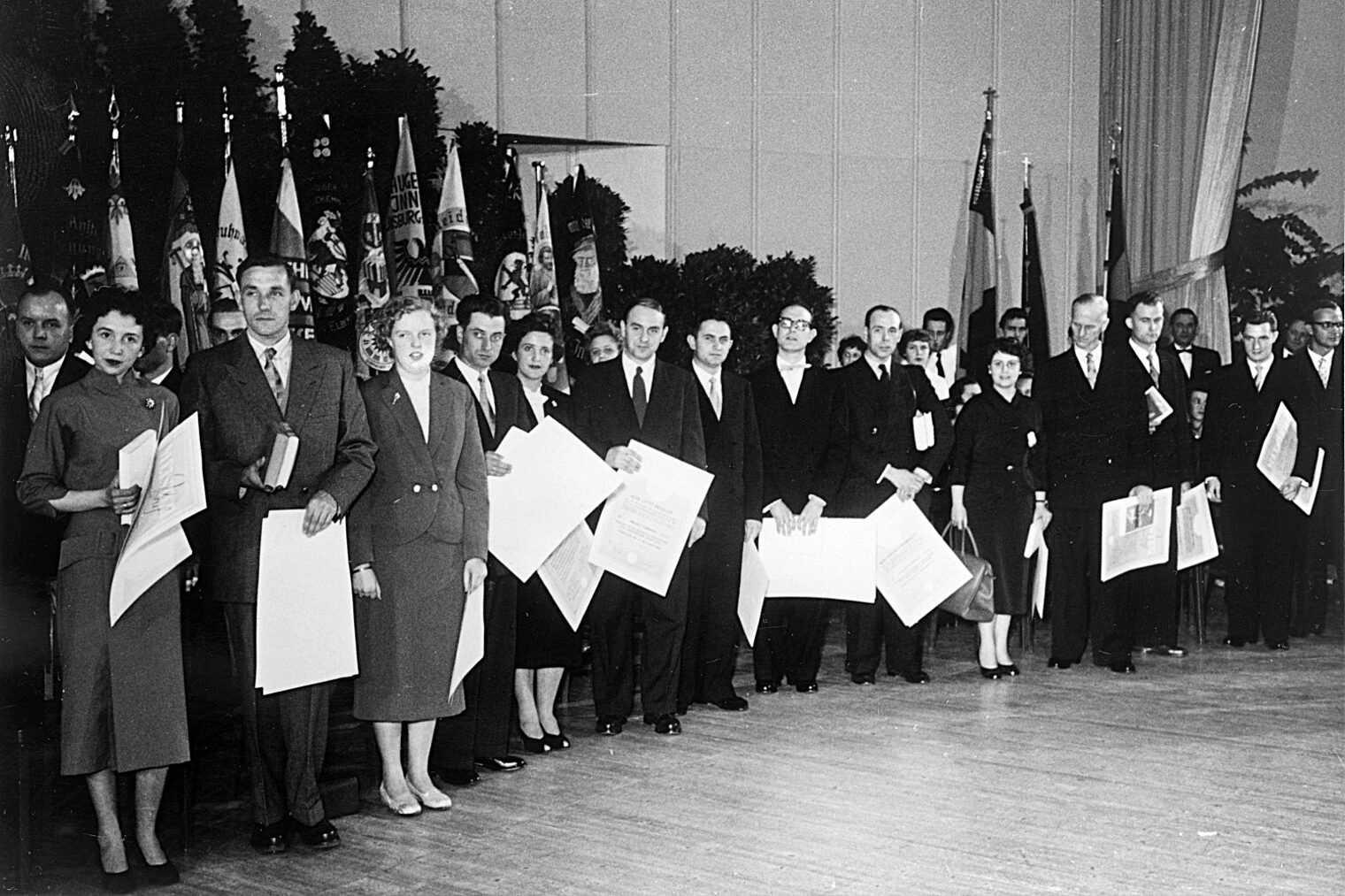 Meisterfeier aus den 60er Jahren: Absolventinnen und Absolventen mit ihren Meisterbriefen stehen auf der Bühne