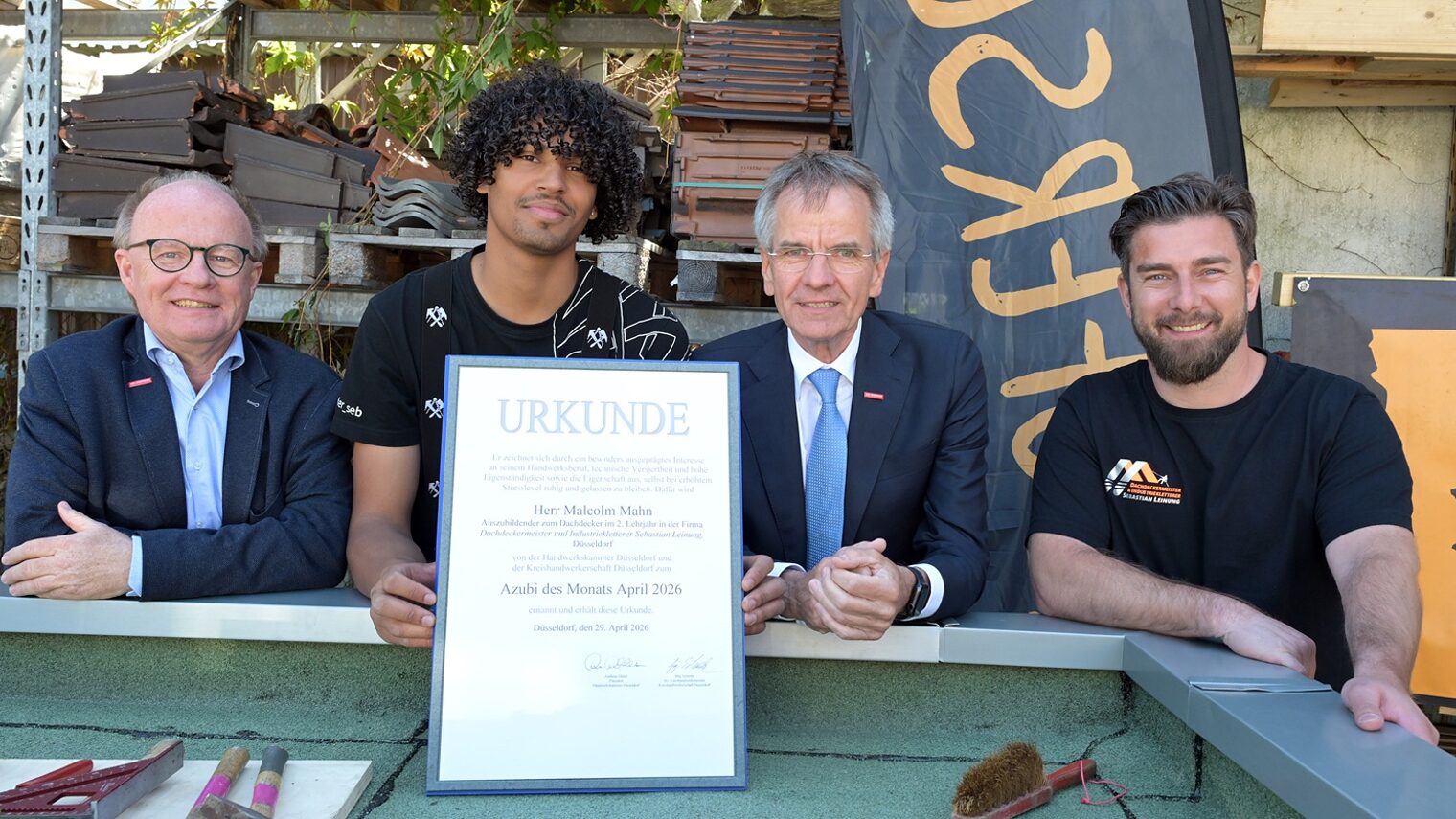 4 Personen posieren für ein Pressefoto. Der frisch ausgezeichnete Azubi des Monats zeigt seine Urkunde.