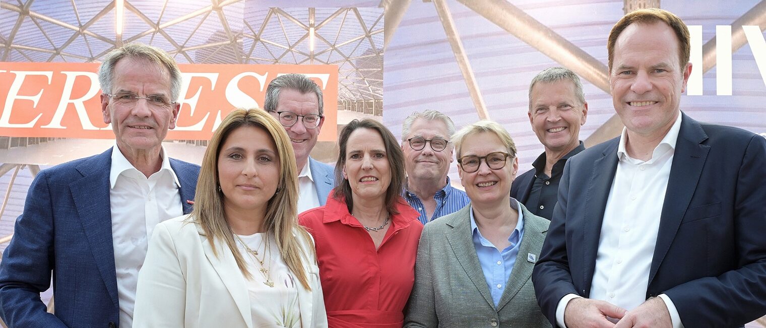 Mehrere Teilnehmende posieren vor einem Hintergrund mit der Schrift Sommerfest für ein Pressefoto.