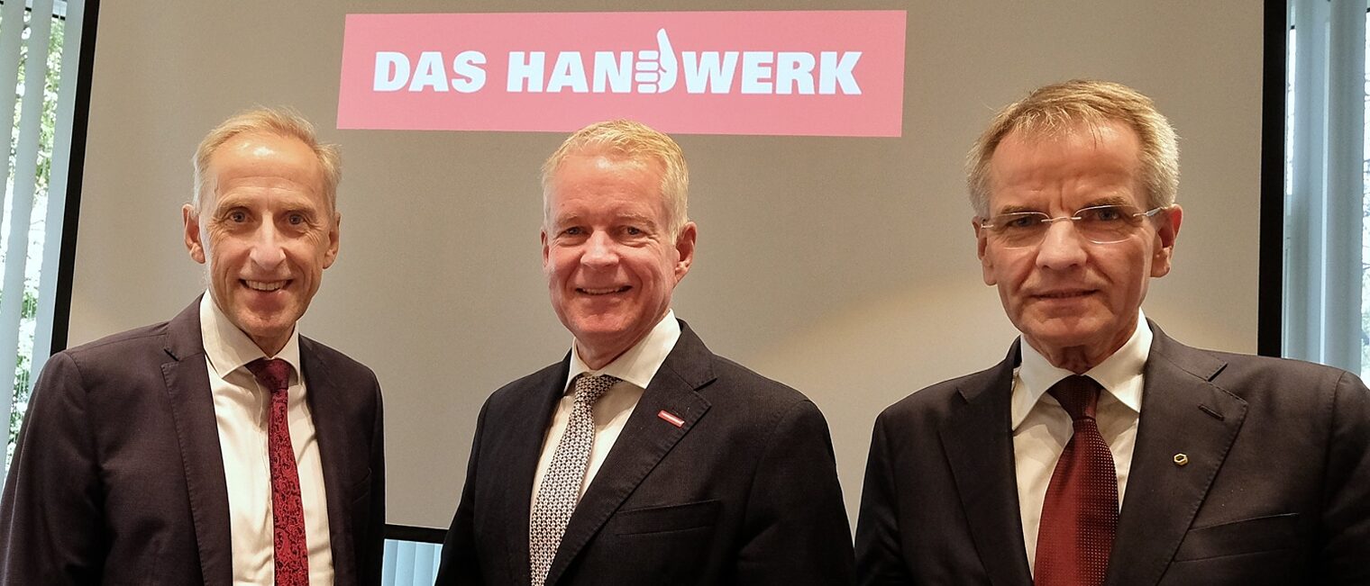 Drei Funktionäre aus dem Handwerk posieren vor einem digitalen Hintergrund.
